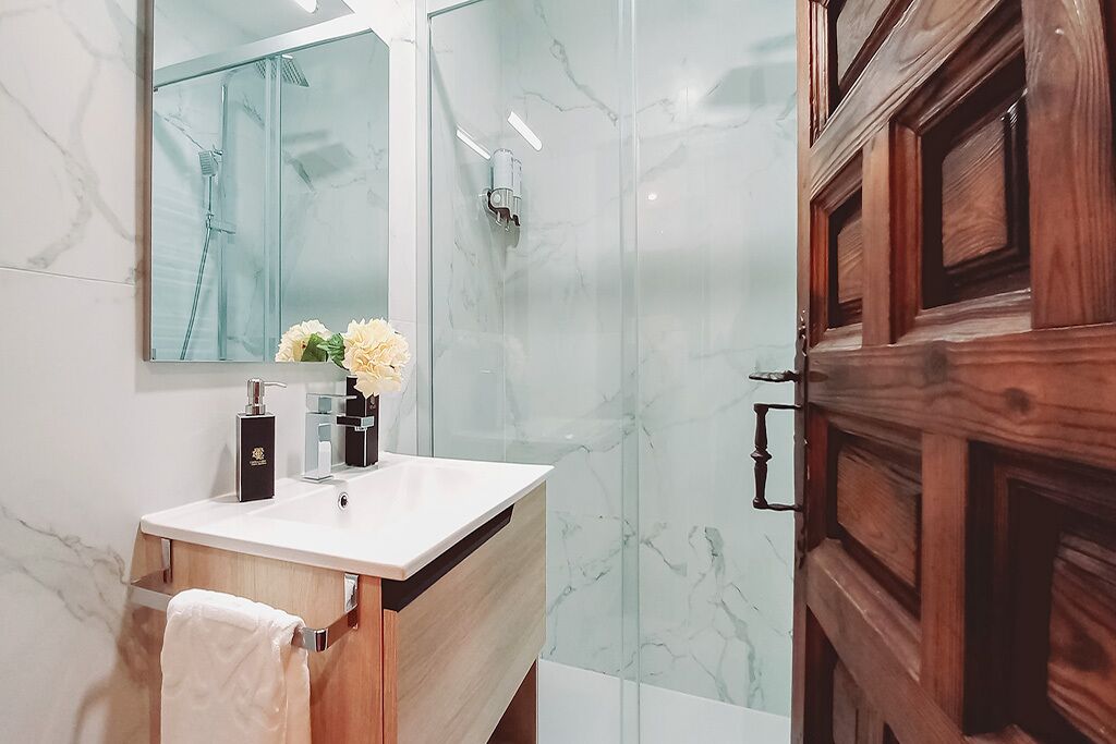 Un baño moderno con ducha de mármol, tocador de madera y un espejo grande.