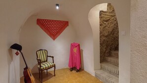 Um quarto com uma cadeira de madeira, um violão, um tecido vermelho e uma parede texturizada.