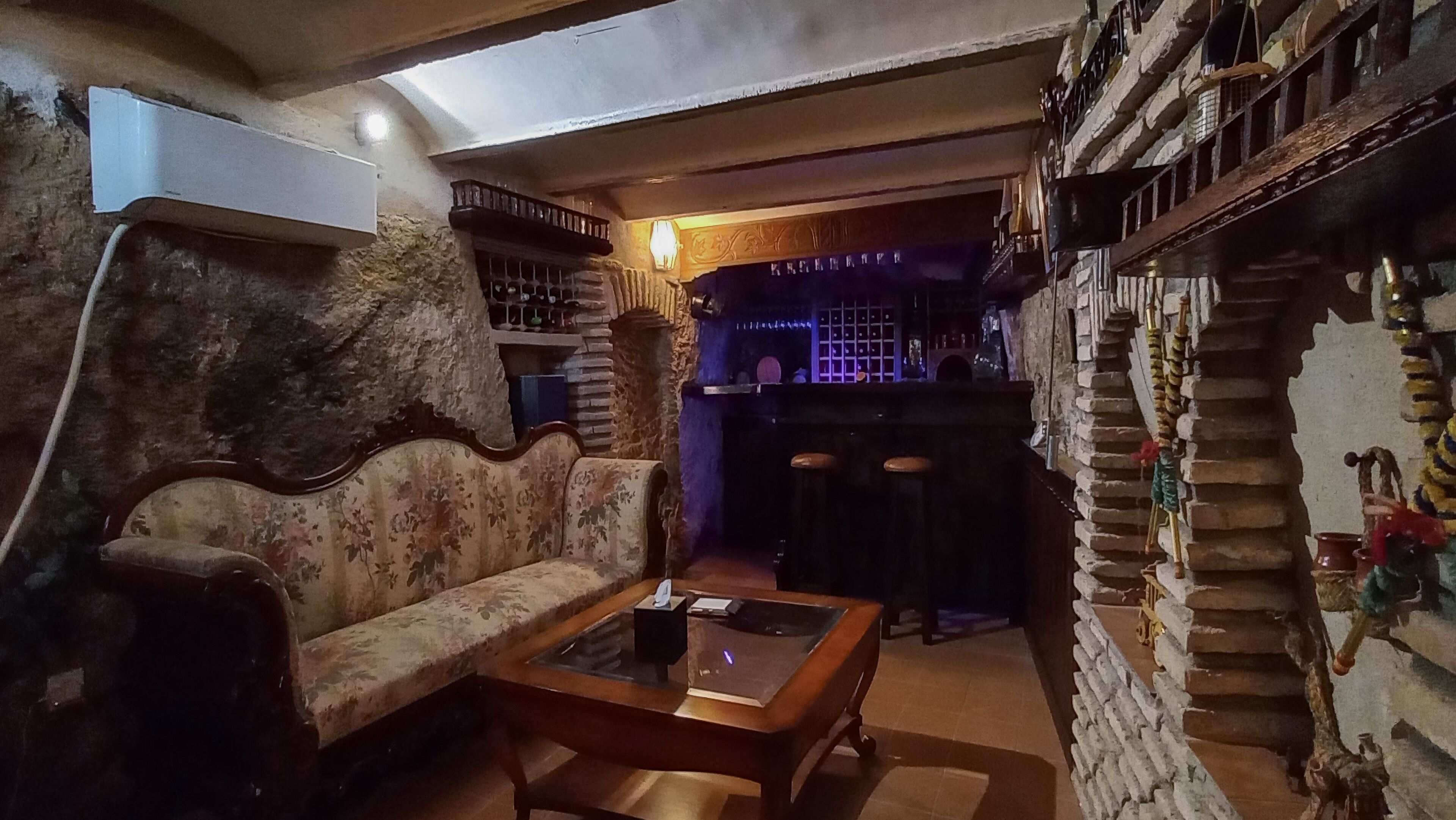 Una habitación acogedora con un sofá antiguo, una mesa de centro de madera, una zona de bar con taburetes y una escalera decorativa.