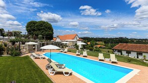 A rectangular swimming pool with a tiled edge, surrounded by a paved deck. There are lounge chairs and umbrellas along the poolside. - Quinta Lusitânia (Santa Comba Dao)