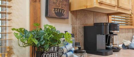 Cuina amb armaris de fusta, una màquina de cafè, una planta en test i un cartell que diu "Tot el que necessites és amor i una bona tassa de cafè."