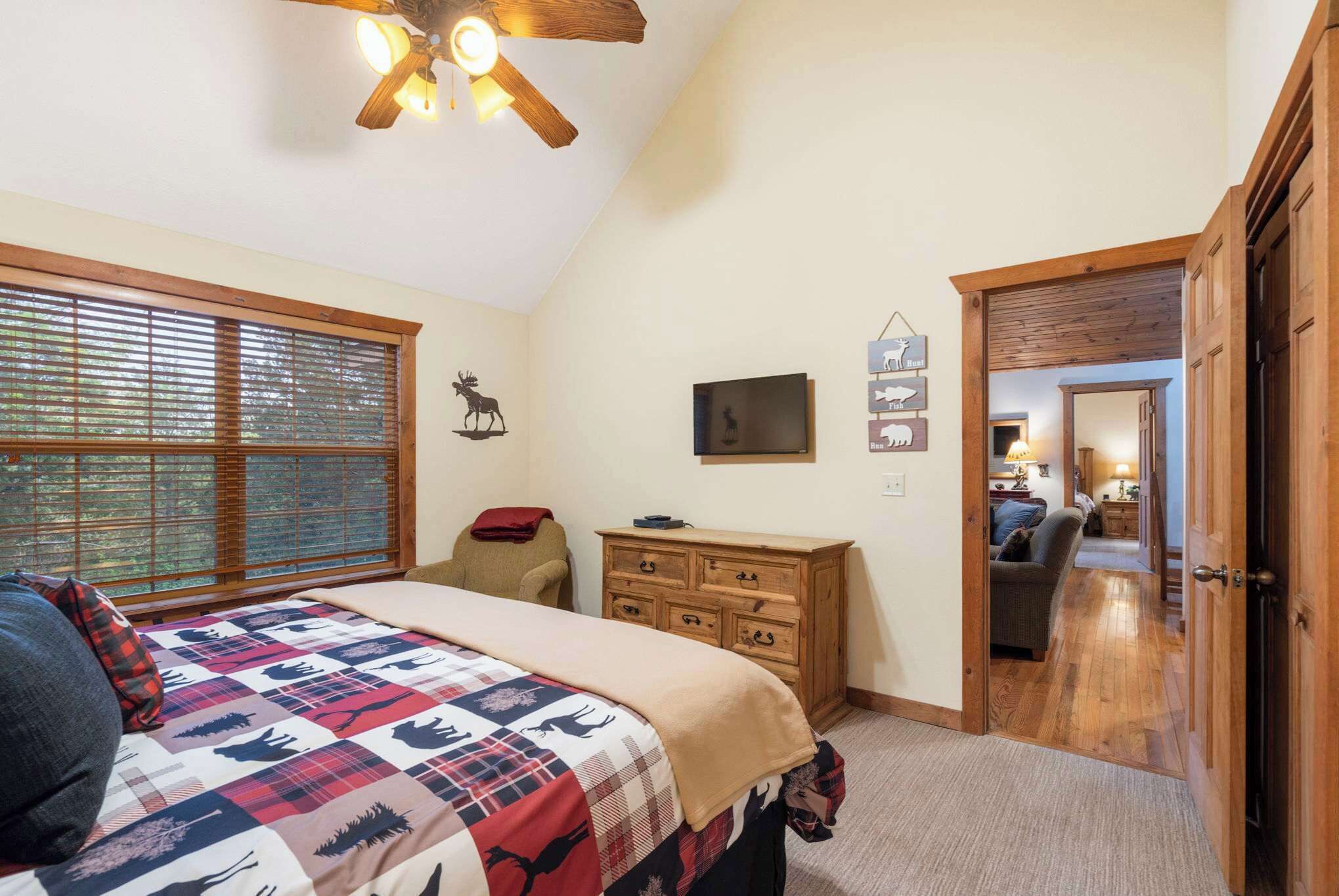A bedroom with a bed, a dresser, a television, and a window with blinds.