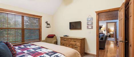 A bedroom with a bed, a dresser, a television, and a window with blinds.