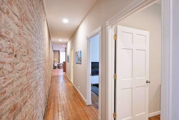 A hallway with a brick wall, wooden flooring, and white doors leading to rooms. - Historic 4BR 3 Kings Sleeps 10 (Cincinnati)
