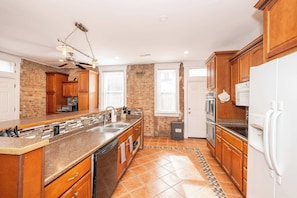 A kitchen with a large island, wooden cabinets, a brick wall, and a tiled floor. - Historic 4BR 3 Kings Sleeps 10 (Cincinnati)
