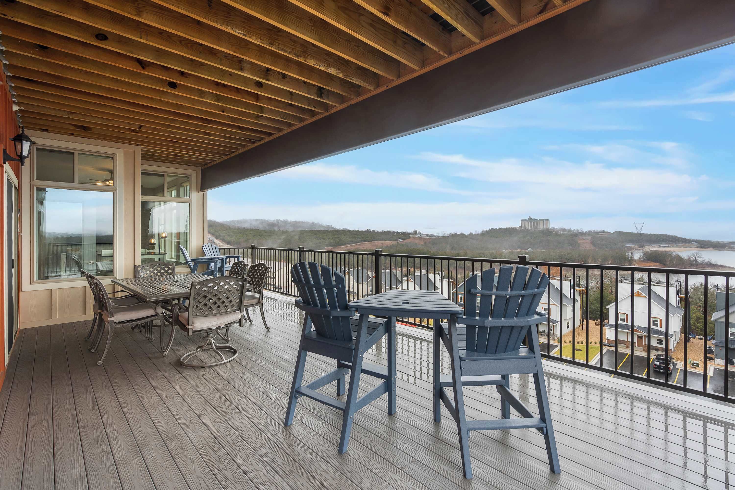 Una terraza de madera con una mesa y sillas, con vista a un paisaje con colinas y un edificio lejano.