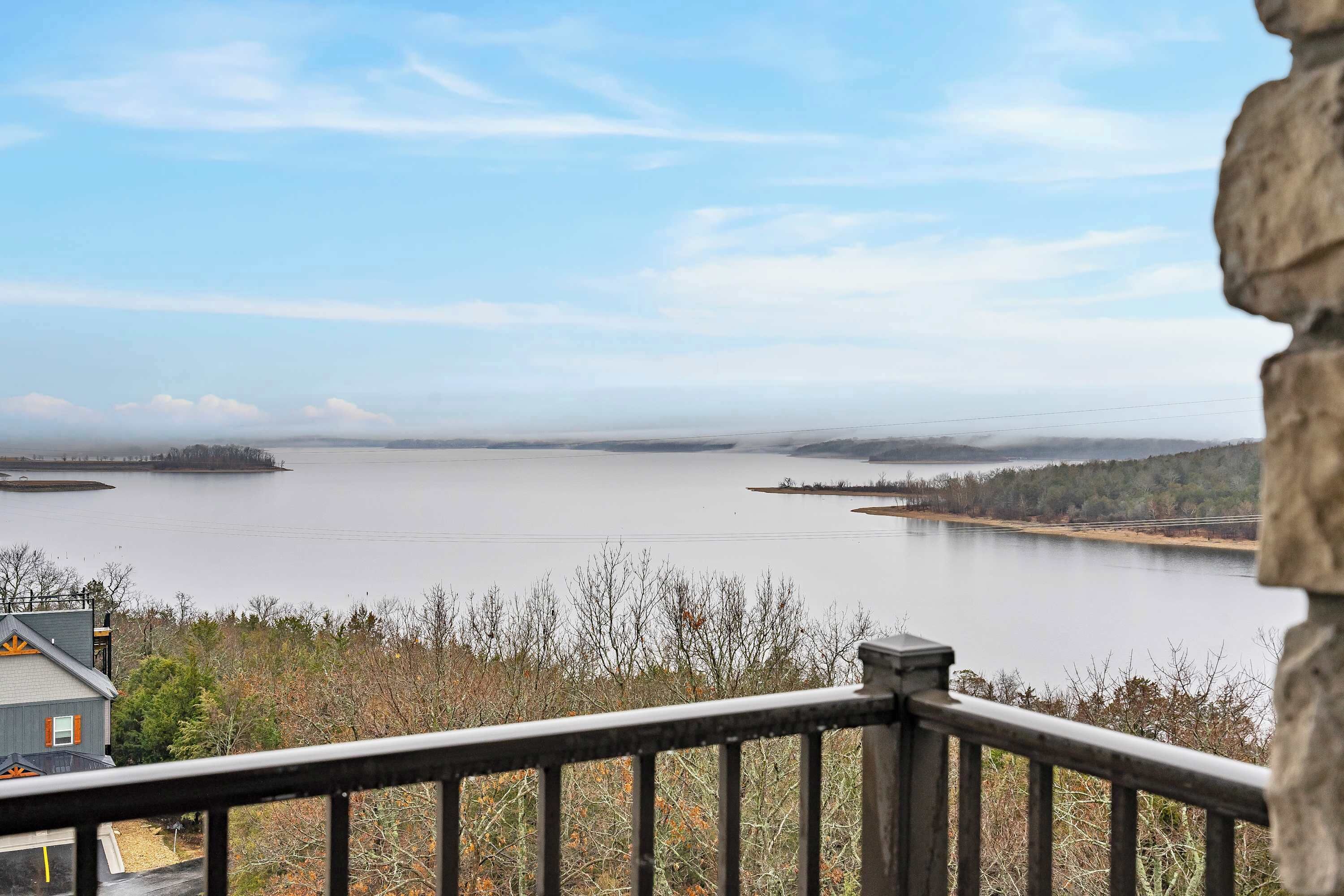 A view of a lake from a balcony with a stone railing, surrounded by trees and a distant shoreline.
