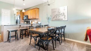 A modern kitchen with wooden cabinets, a central island, and a dining area with a table and chairs. - Sunset Daydream Elegant Condo on Table Rock! (Branson)