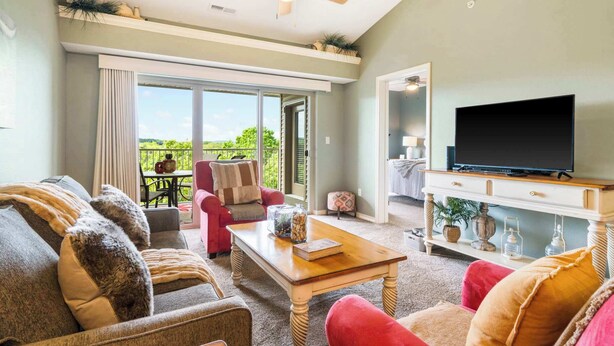 A living room with a sofa, armchair, and coffee table, a flat-screen TV on a stand, and a ceiling fan. - Sunset Daydream Elegant Condo on Table Rock! (Branson)
