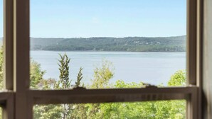 A view through a window of a lake with a forested shoreline and distant hills. - Sunset Daydream Elegant Condo on Table Rock! (Branson)