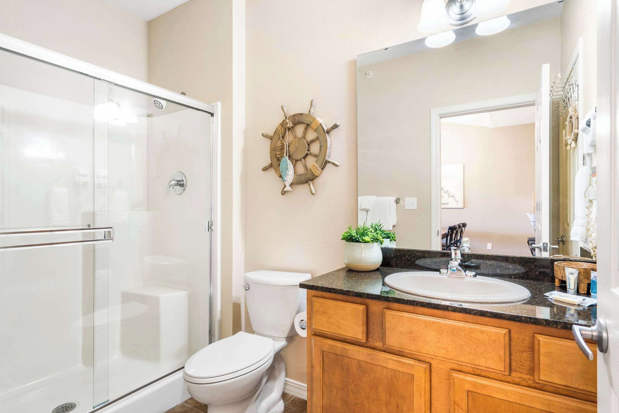 Une salle de bain avec une douche à parois de verre, des toilettes blanches, un meuble-lavabo en bois et un grand miroir.