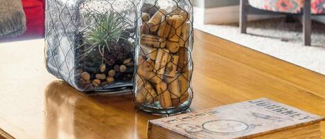 Two glass containers with wire frames, one filled with corks and the other with pebbles and a plant, on a wooden table with a book beside them.