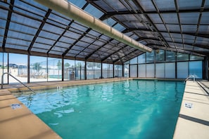 An indoor swimming pool with clear blue water, surrounded by a covered area with large windows and a view of the outside. - Honey Hill - Pet Friendly - Indoor Pool (Branson)