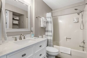 Ein Badezimmer mit einem Doppelwaschbecken, Toilette, Dusche mit Duschbrausehandstück und Handtuchhalter.