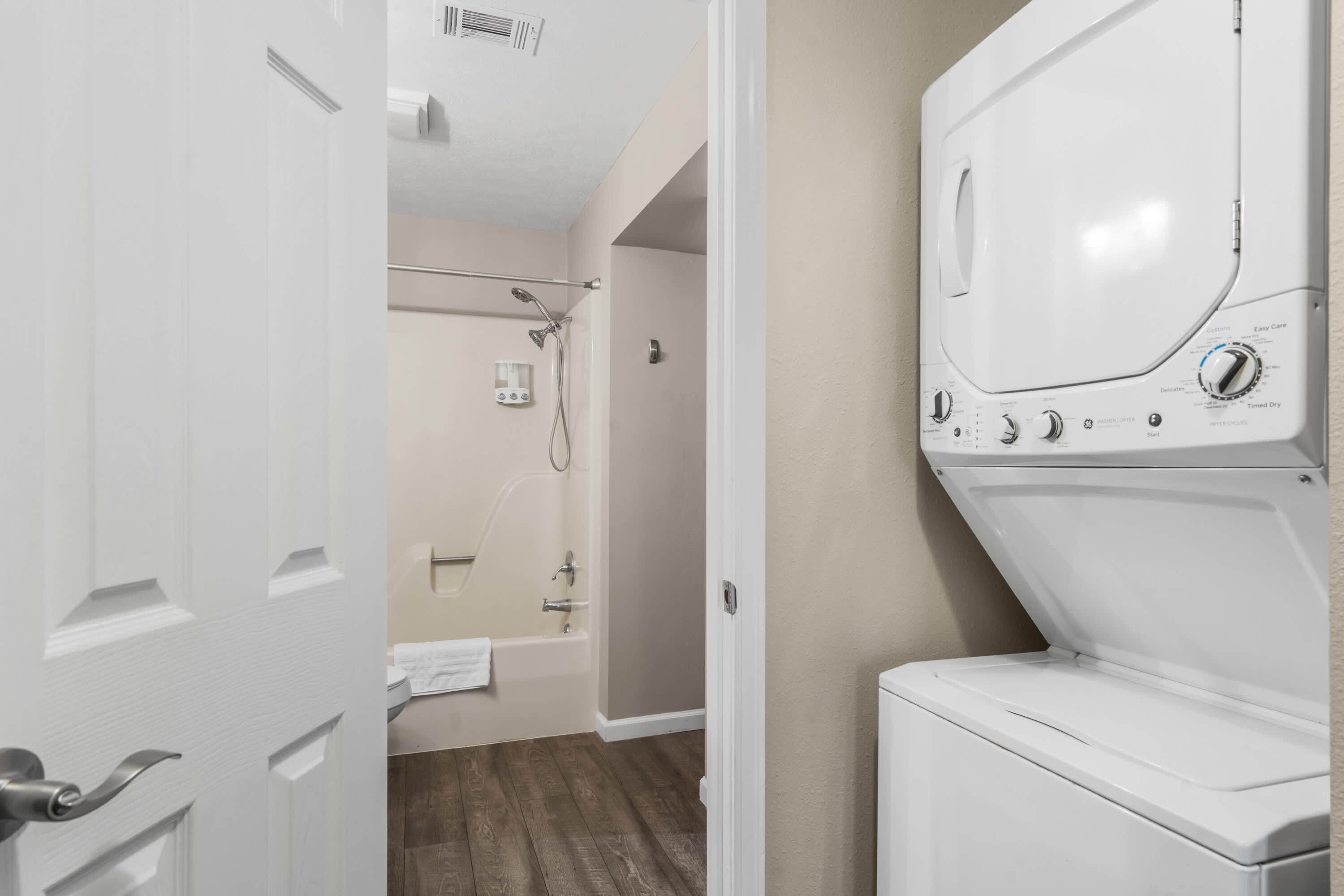 A laundry room with a front-loading washer and dryer, a shower with a handheld showerhead, and a bathtub.