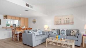 A modern living room with a grey sofa, a coffee table, and a dining area with wooden chairs and a table.