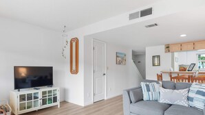 A modern living room with a flat-screen TV, a grey sofa, and a coffee table with colorful glassware.