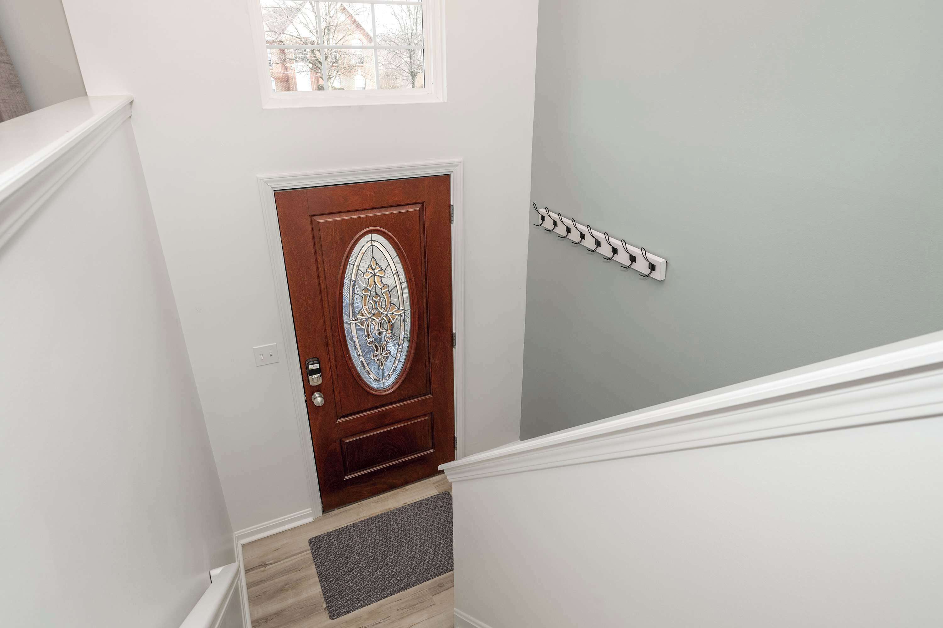 A staircase with a wooden door featuring a stained glass window, a white wall, and a light gray wall with a white baseboard.