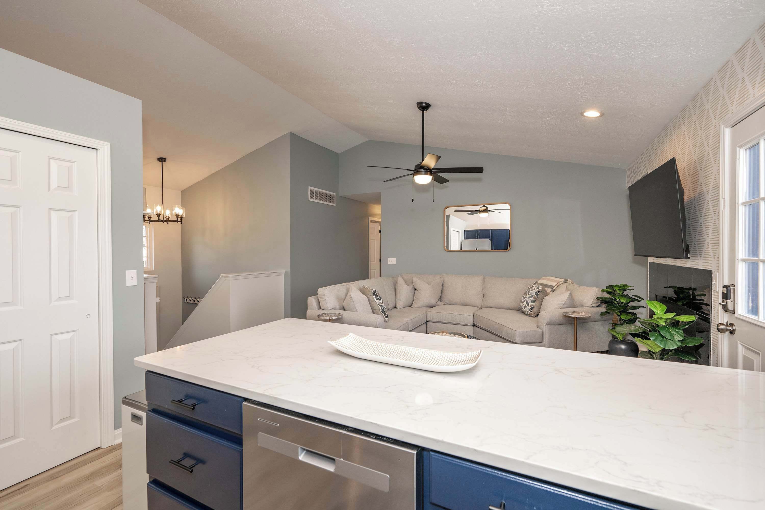 A modern kitchen with a marble countertop, built-in dishwasher, and a ceiling fan.