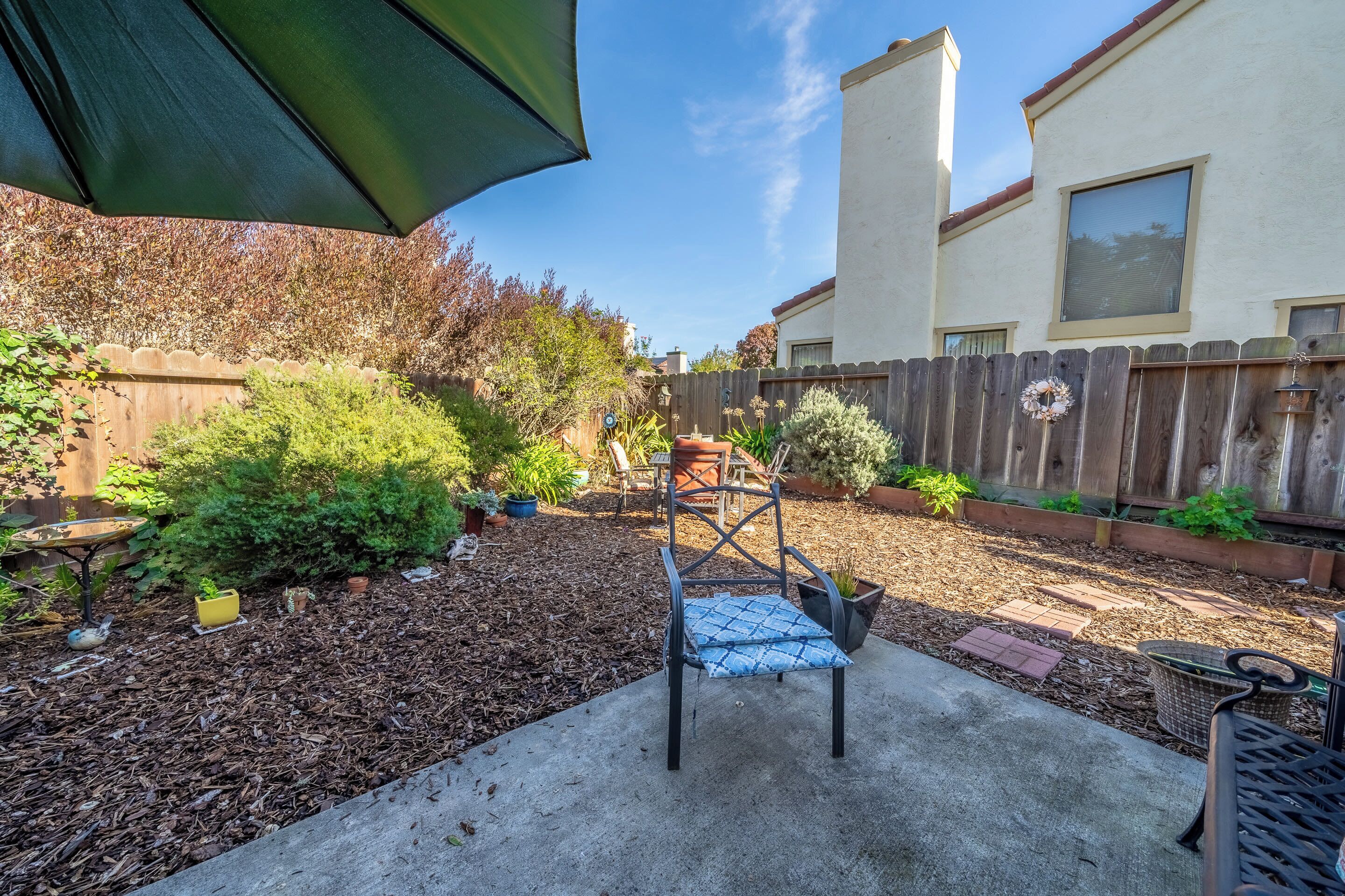 A backyard with a patio area, a wooden fence, and various plants.