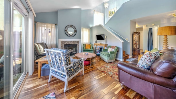 A spacious living room with a fireplace, a staircase, and a large window. - Succulents & Seashells Coastal Paradise by Beach (Marina)