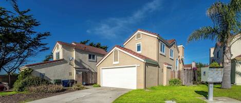 A residential neighborhood with houses featuring red-tiled roofs and beige walls, a well-maintained lawn, and a clear blue sky.