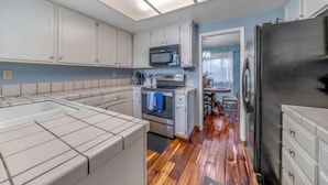 A kitchen with white cabinets, a stainless steel oven, a microwave, and a black refrigerator. - Succulents & Seashells Coastal Paradise by Beach (Marina)