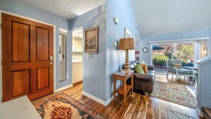 A spacious living area with hardwood flooring, a large wooden door, and a view to a patio with outdoor furniture. - Succulents & Seashells Coastal Paradise by Beach (Marina)