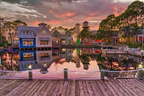 A waterfront area with buildings reflecting on the water, a wooden dock, and a bridge. - Sandestin Bungalo 45: Golf Cart, Pool, & More! (Miramar Beach)