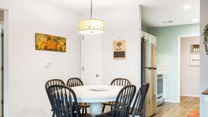 Een eetgedeelte met een witte tafel en zwarte stoelen, een schilderij aan de muur, een WiFi-bordje en een koelkast op de achtergrond.