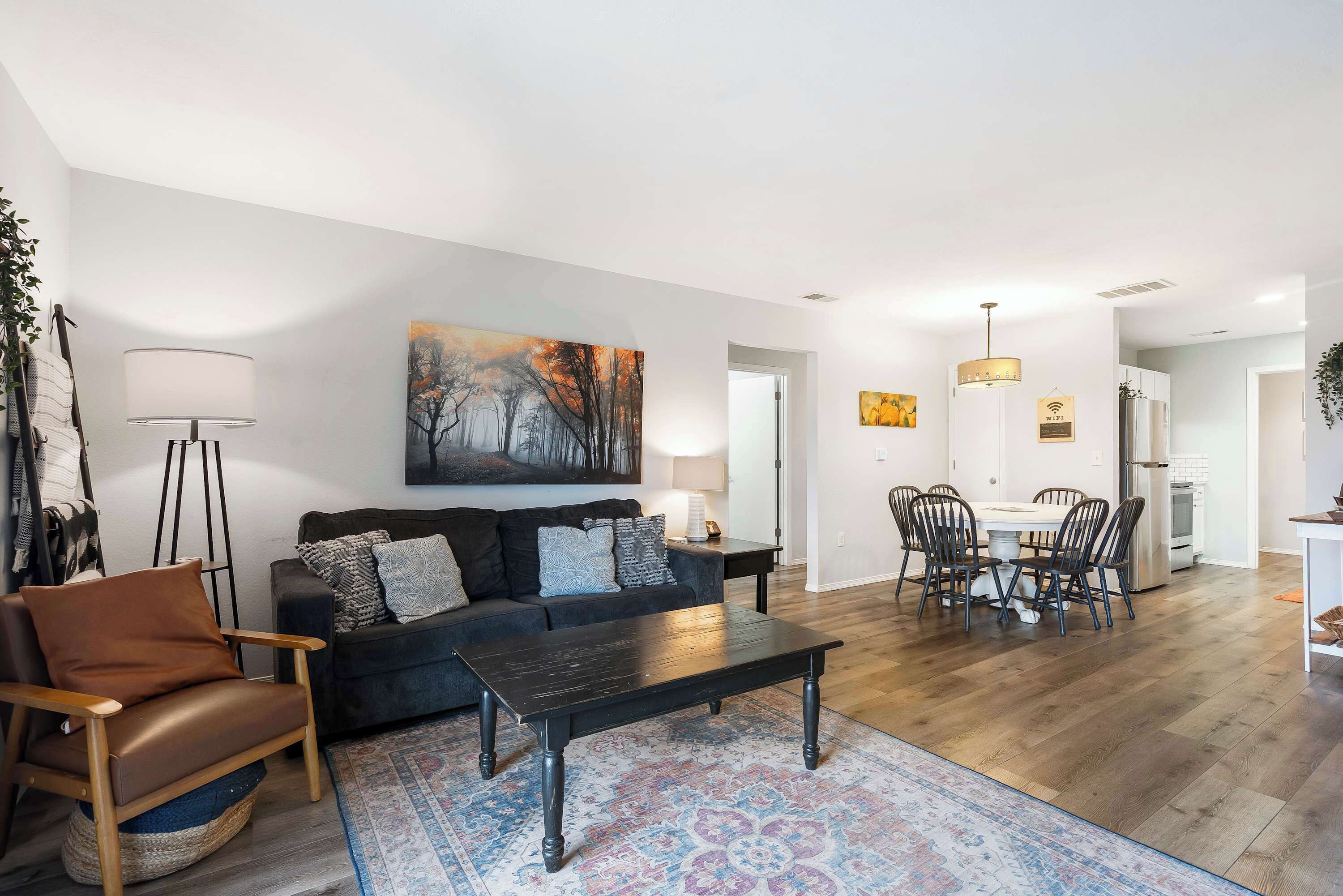 A modern living room with a sofa, armchair, coffee table, and dining area with chairs and a table.