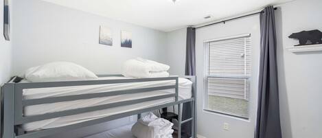 A bunk bed room with a window and a bear decoration on the wall.