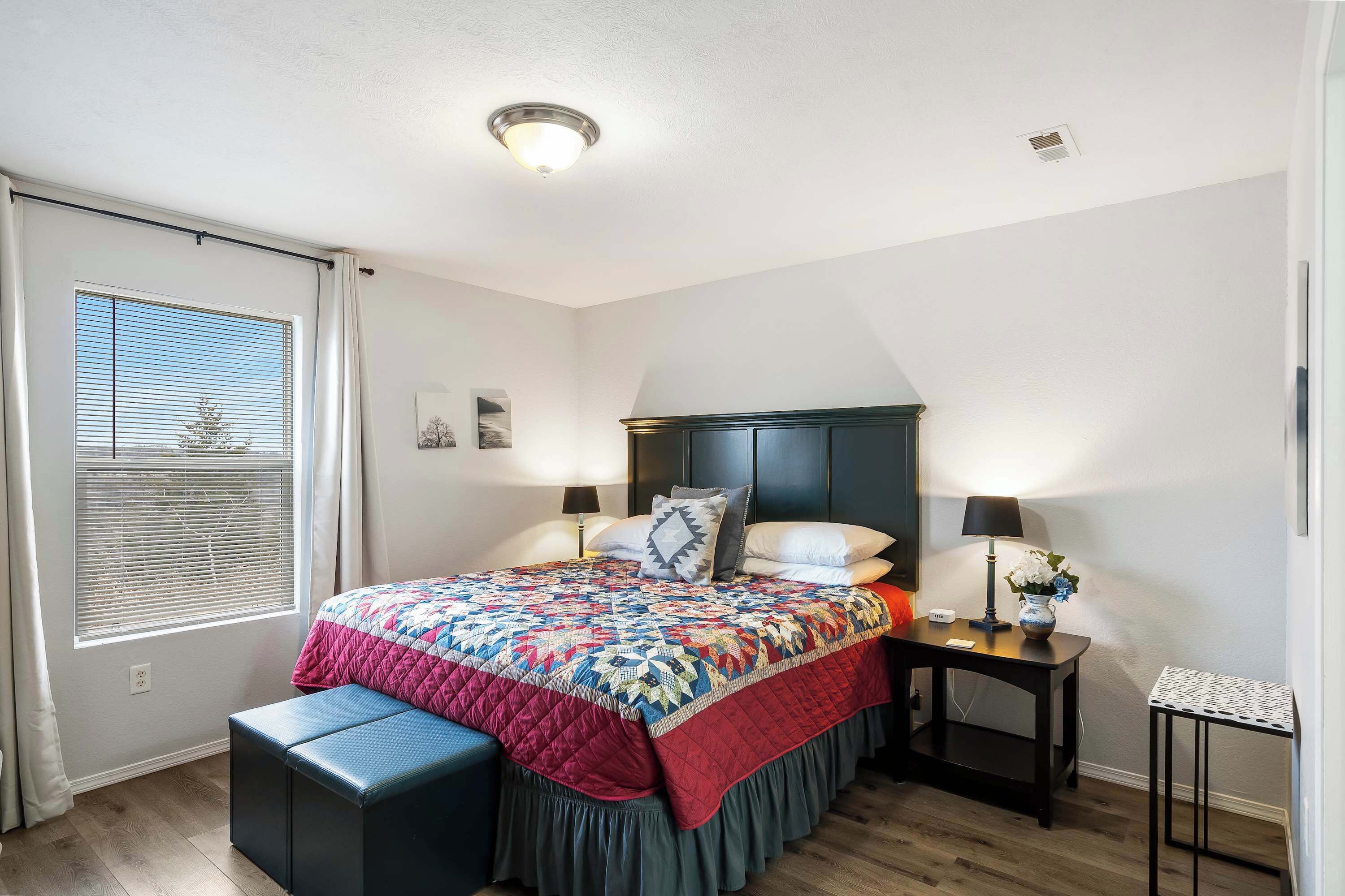 Ein Schlafzimmer mit Bett, Nachttischen, einem Fenster mit Jalousien und einer Deckenleuchte.