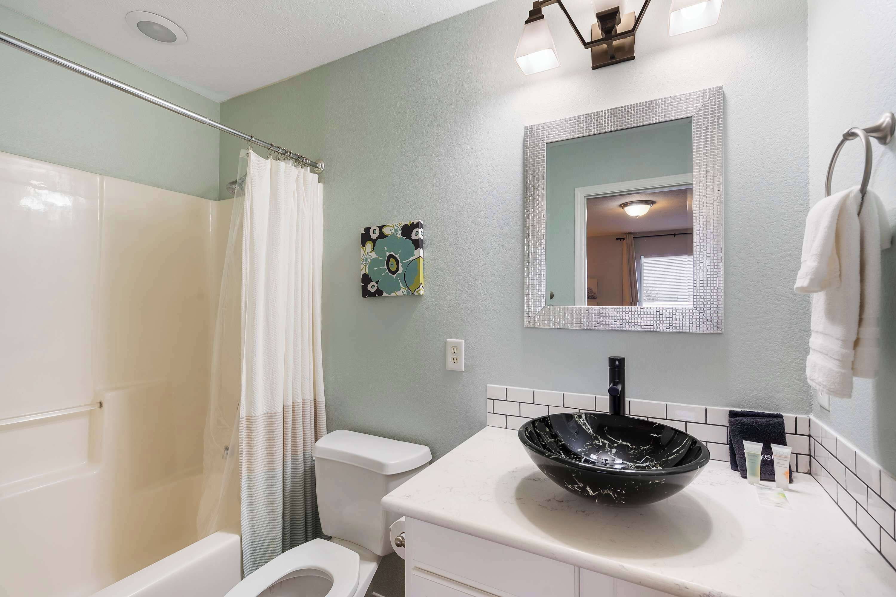 A bathroom with a shower, toilet, sink with a black basin, and a mirror with a decorative frame.