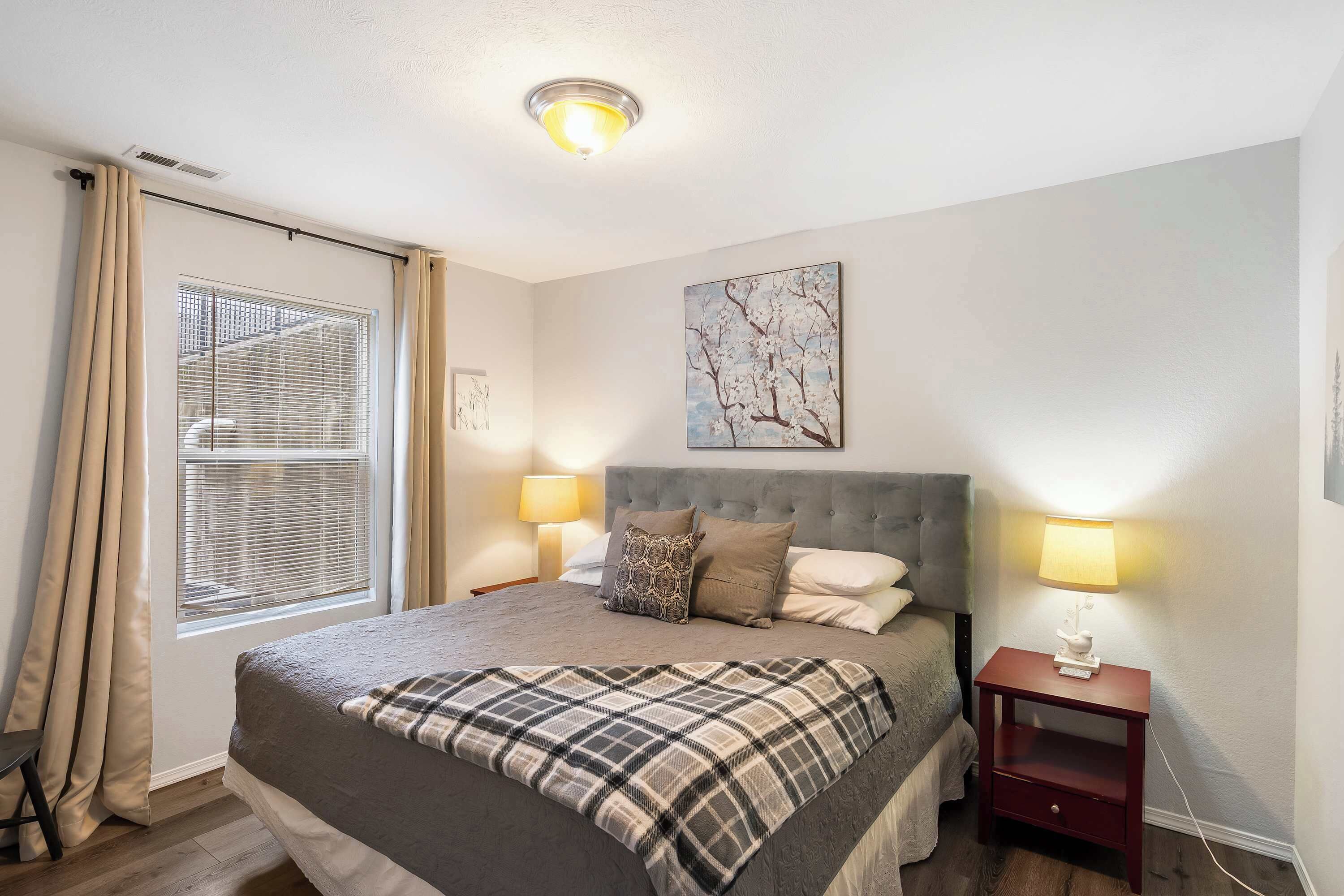 A neatly arranged bedroom with a bed, bedside lamps, a nightstand, and a window with blinds.