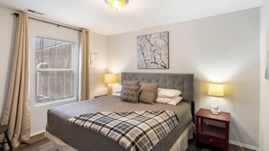 Een keurig opgemaakt slaapkamer met een bed, nachtlampjes, een nachtkastje en een raam met jaloezieën.