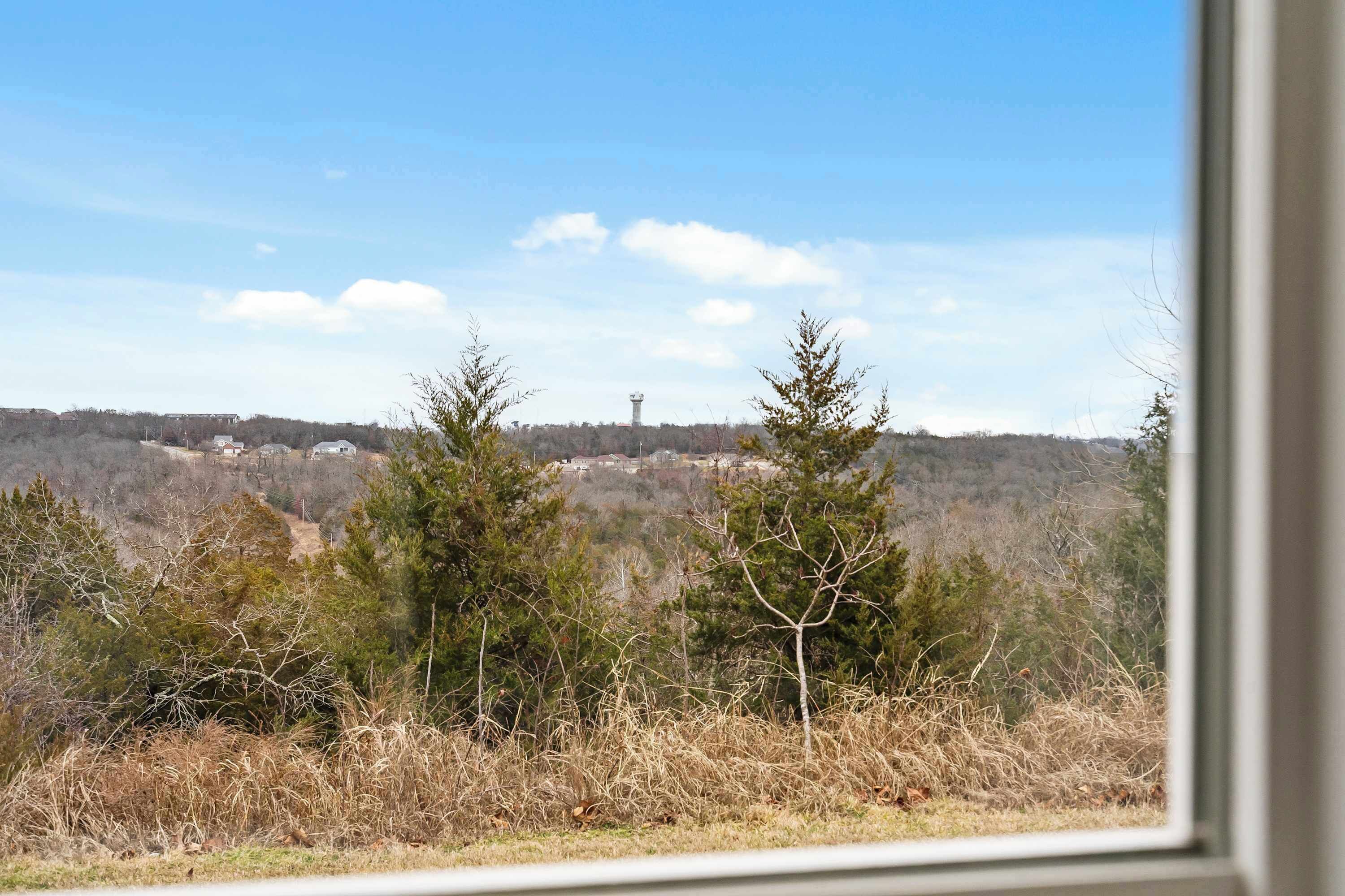 A view from a window overlooking a landscape with trees and a distant tower.
