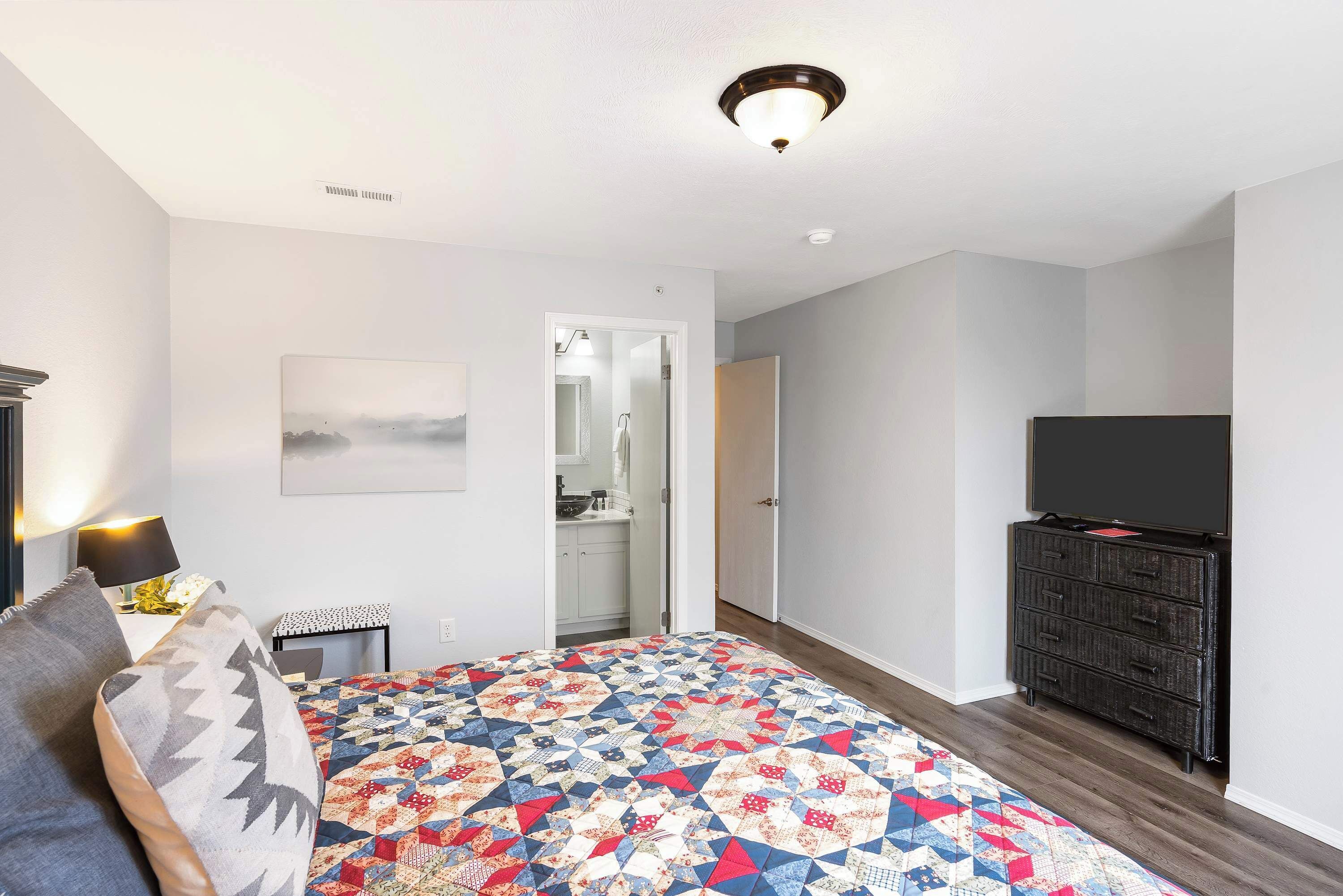 A bedroom with a bed, a dresser, a television, and a bathroom door.