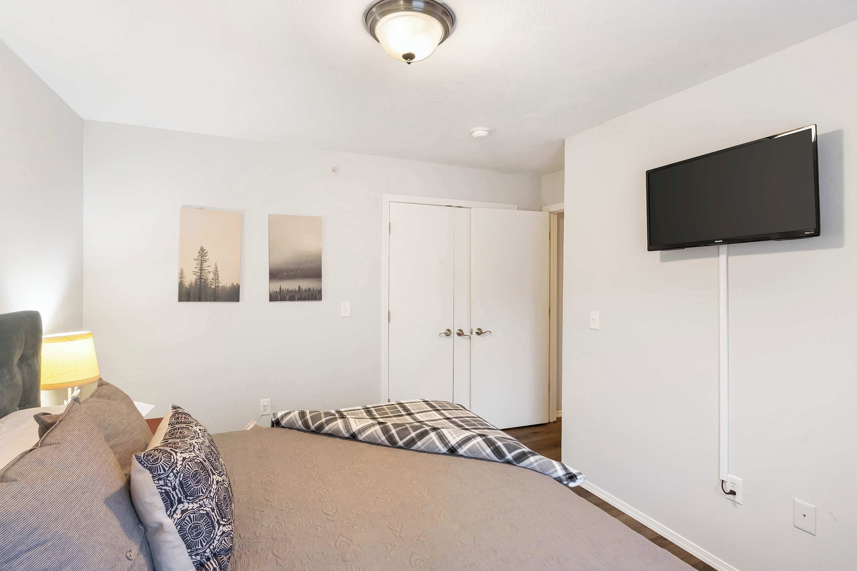 A bedroom with a bed, a television mounted on the wall, and a door with a white frame.