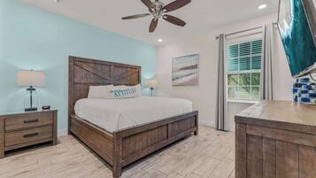 A bedroom with a wooden bed, a ceiling fan, a nightstand, a lamp, a window with blinds, and a painting on the wall.