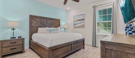 A bedroom with a wooden bed, a ceiling fan, a nightstand, a lamp, a window with blinds, and a painting on the wall.