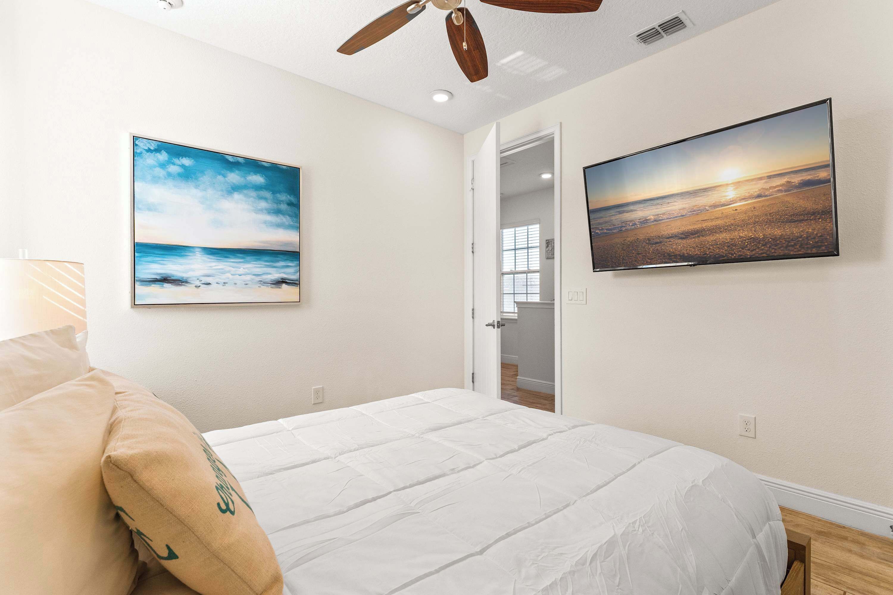 Quarto com cama, ventilador de teto, televisão e duas pinturas nas paredes.