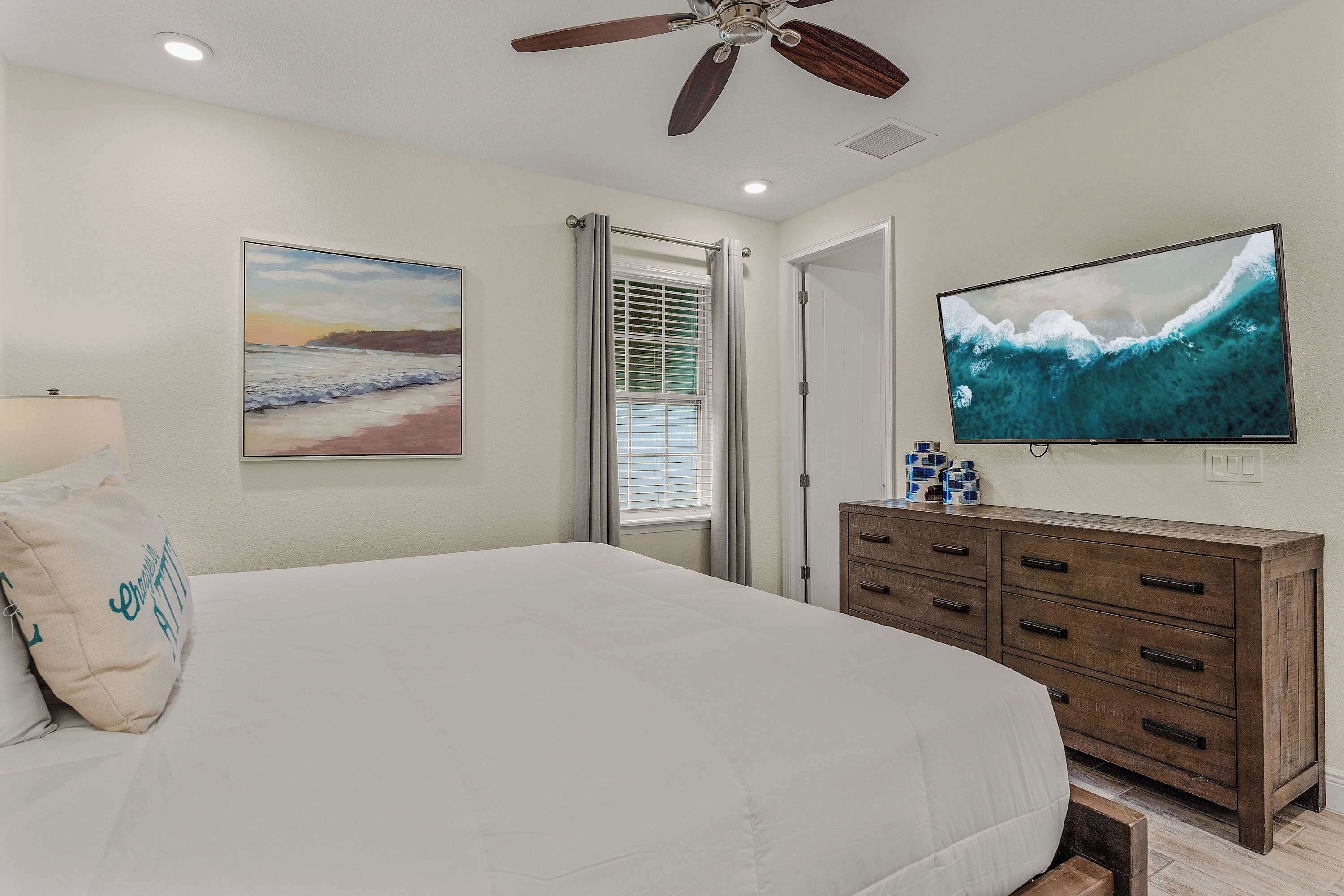 A bedroom with a bed, a ceiling fan, a TV, a dresser, and a window with blinds.