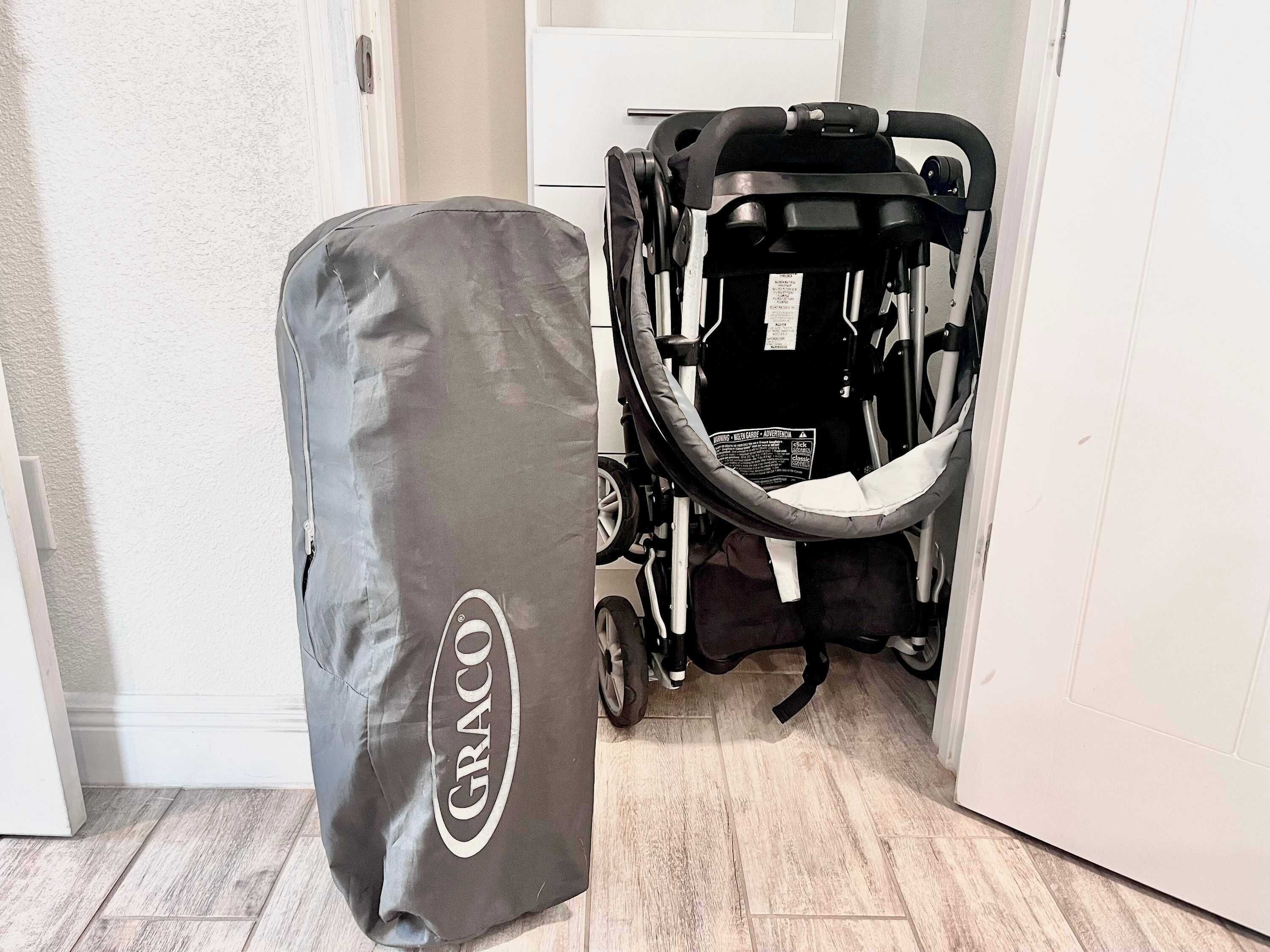 A Graco stroller in a hallway with a grey carrying bag beside it.