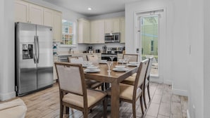 A modern kitchen with white cabinets, stainless steel appliances, and a dining area with a wooden table and chairs. - Frankly Fintastic (Kissimmee)
