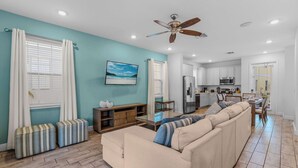A spacious living room with a beige sofa, striped ottomans, and a ceiling fan. - Frankly Fintastic (Kissimmee)