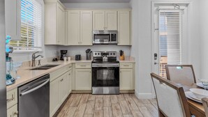 A kitchen with white cabinets, stainless steel appliances, a dishwasher, and a dining area with a table and chairs. - Frankly Fintastic (Kissimmee)