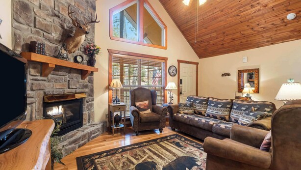 A cozy living room with a stone fireplace, wooden ceiling, and a comfortable seating area. - Creekside - 2 BDR Resort Cabin in Epic Location! (Branson West)