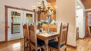 A dining area with a wooden table and chairs, a chandelier, and a view of the kitchen through a glass door. - Creekside - 2 BDR Resort Cabin in Epic Location! (Branson West)