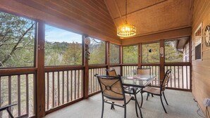 A covered outdoor dining area with a table and chairs, wooden railings, and a view of trees and hills. - Creekside - 2 BDR Resort Cabin in Epic Location! (Branson West)
